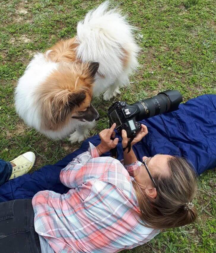 Fotografin liegt mit Kamera am Boden. Hund bescchnüffelt die Kamera