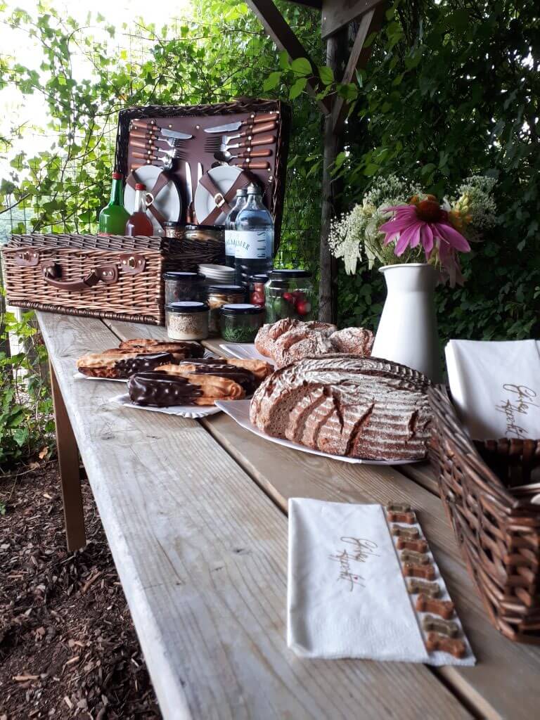 Picknick mit Hund. Gedeckter Holztisch mit Brot, Gebäck und Picknickkorb.